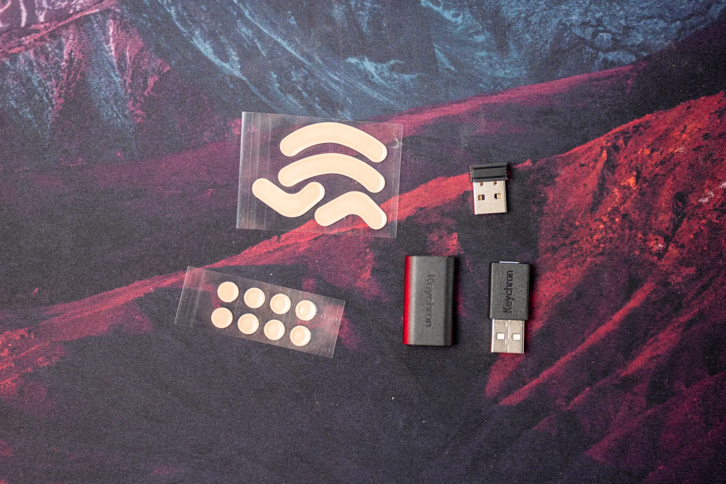 Two types of extra skates, the 2.4 GHz receiver, an extender and a USB-A to USB-C adapter on a mousepad