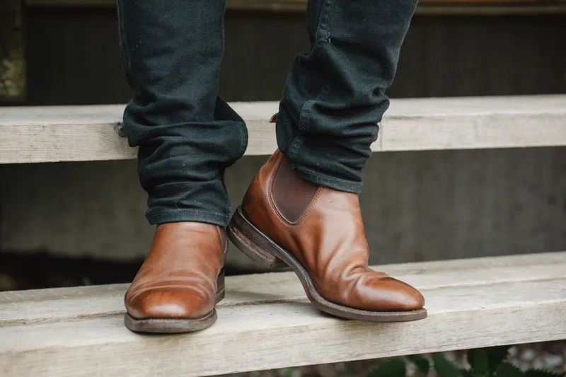 R.M. Williams Comfort Craftsman in brown, worn with dark jeans, heel lifted mid step on wooden steps