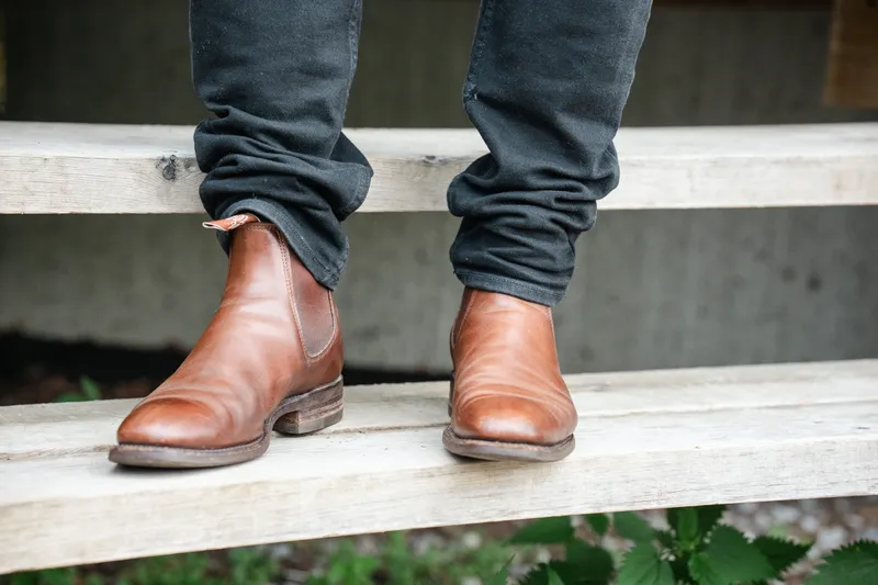 R.M. Williams Comfort Craftsman in brown, worn with dark jeans, front view standing on wooden steps