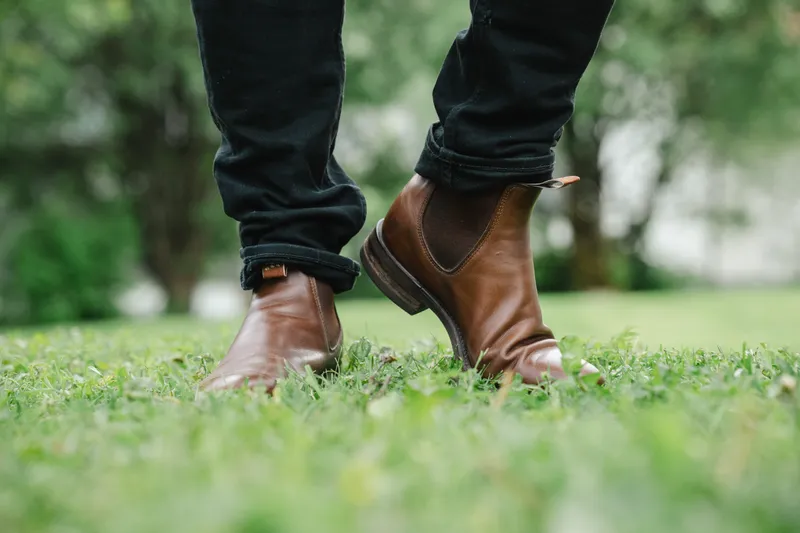 Brown R.M. Williams Comfort Craftsman worn with black jeans, low angle on green grass