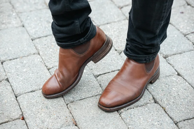 Brown R.M. Williams Comfort Craftsman worn with black jeans, toes forward on cobblestone