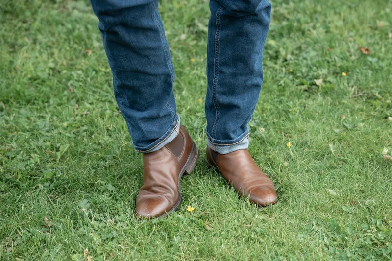 Brown R.M. Williams Comfort Craftsman worn with blue jeans, standing on grass