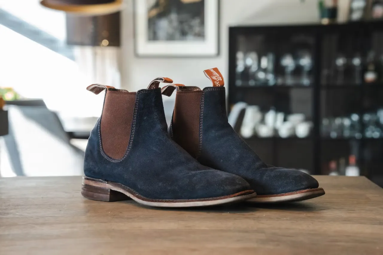 My blue suede pair of R.M. Williams seen at an angle from the front on a wooden table