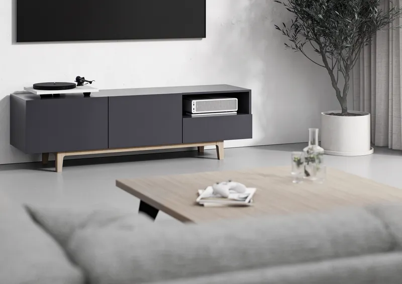 The same white console-style PC in a full living-room scene, under a wall-mounted TV beside a turntable
