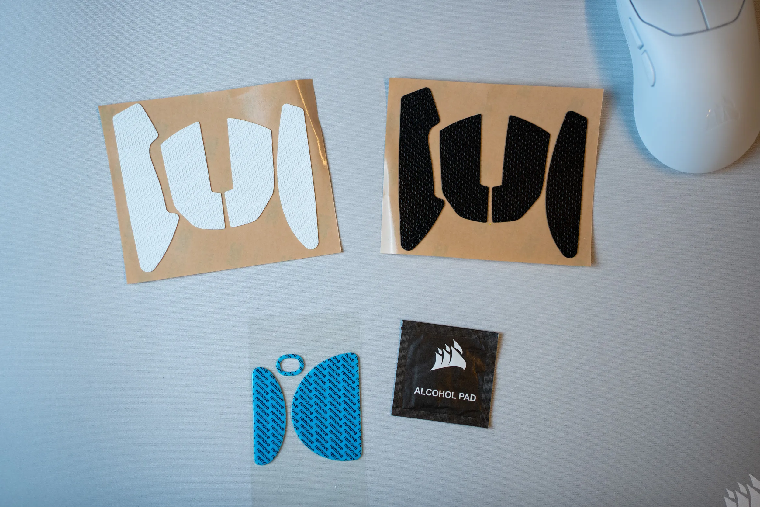 Grip tape in white and black, a set of blue mouse feet and an alcohol pad from the Sabre v3 Pro PureVector box, next to the white mouse