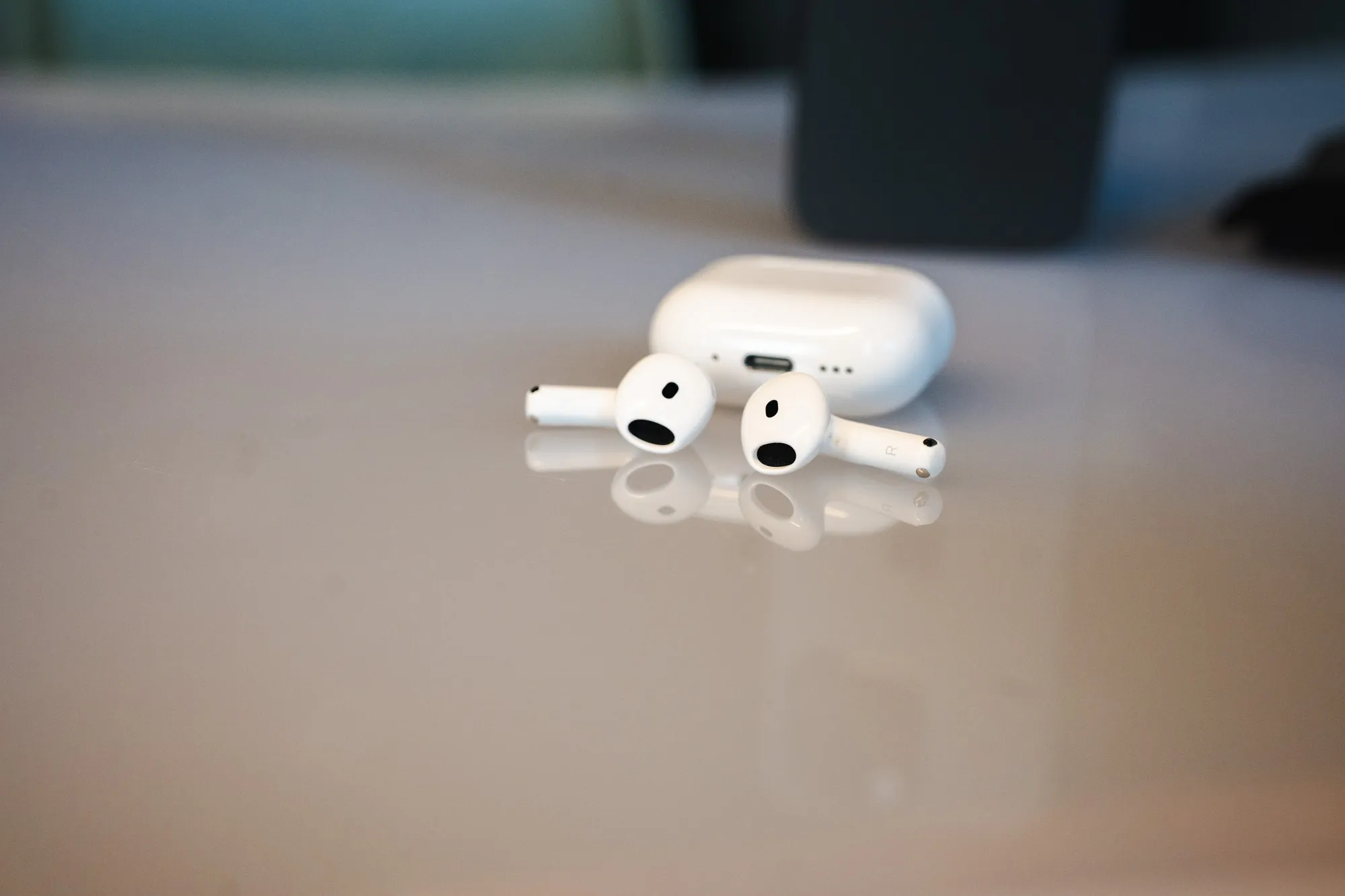 Both AirPods 5 earbuds lying in front of the case on a glossy table, with the USB-C port visible on the case