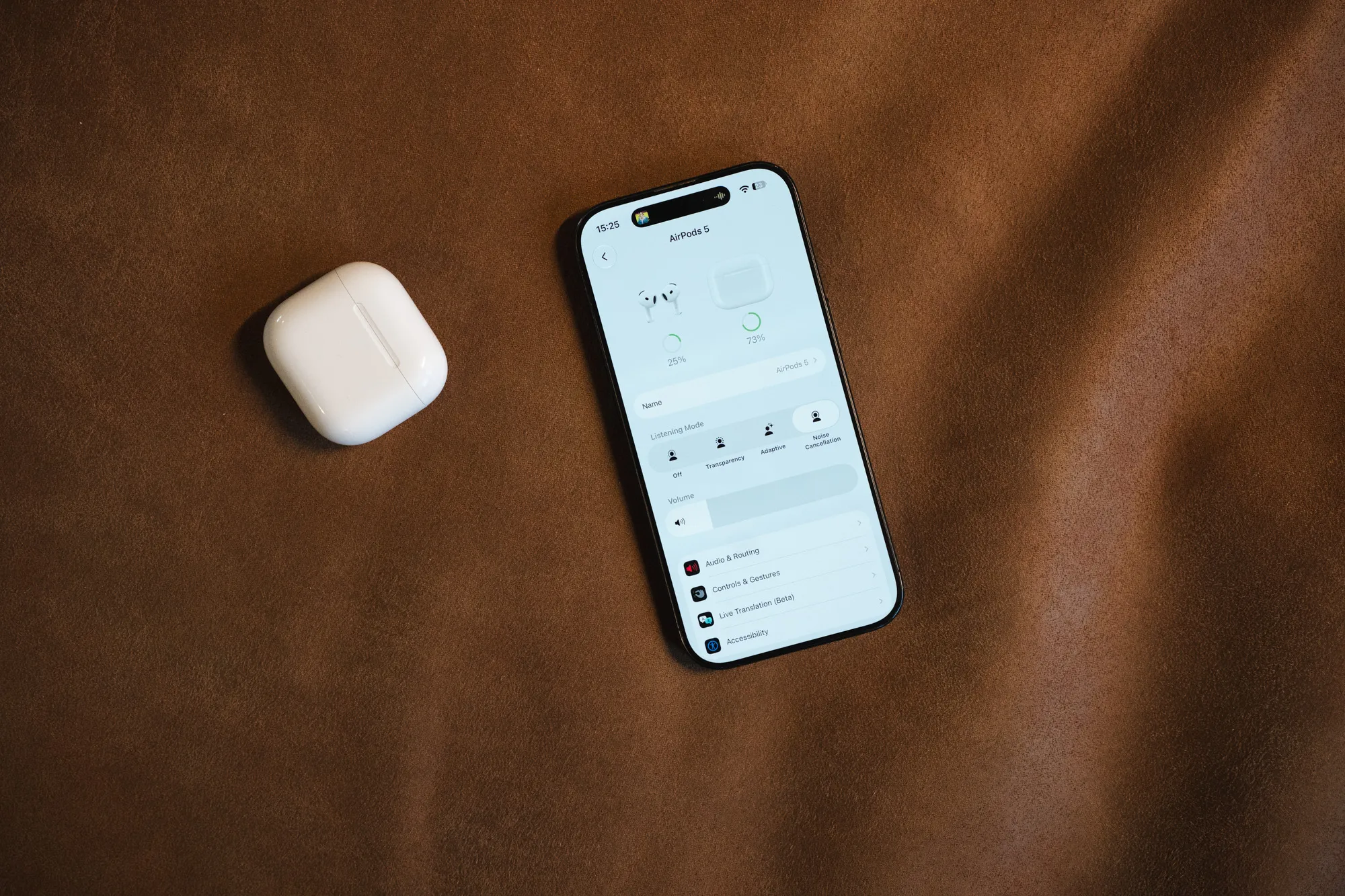 The AirPods 5 case and an iPhone with the AirPods settings on a brown leather mat, seen from above
