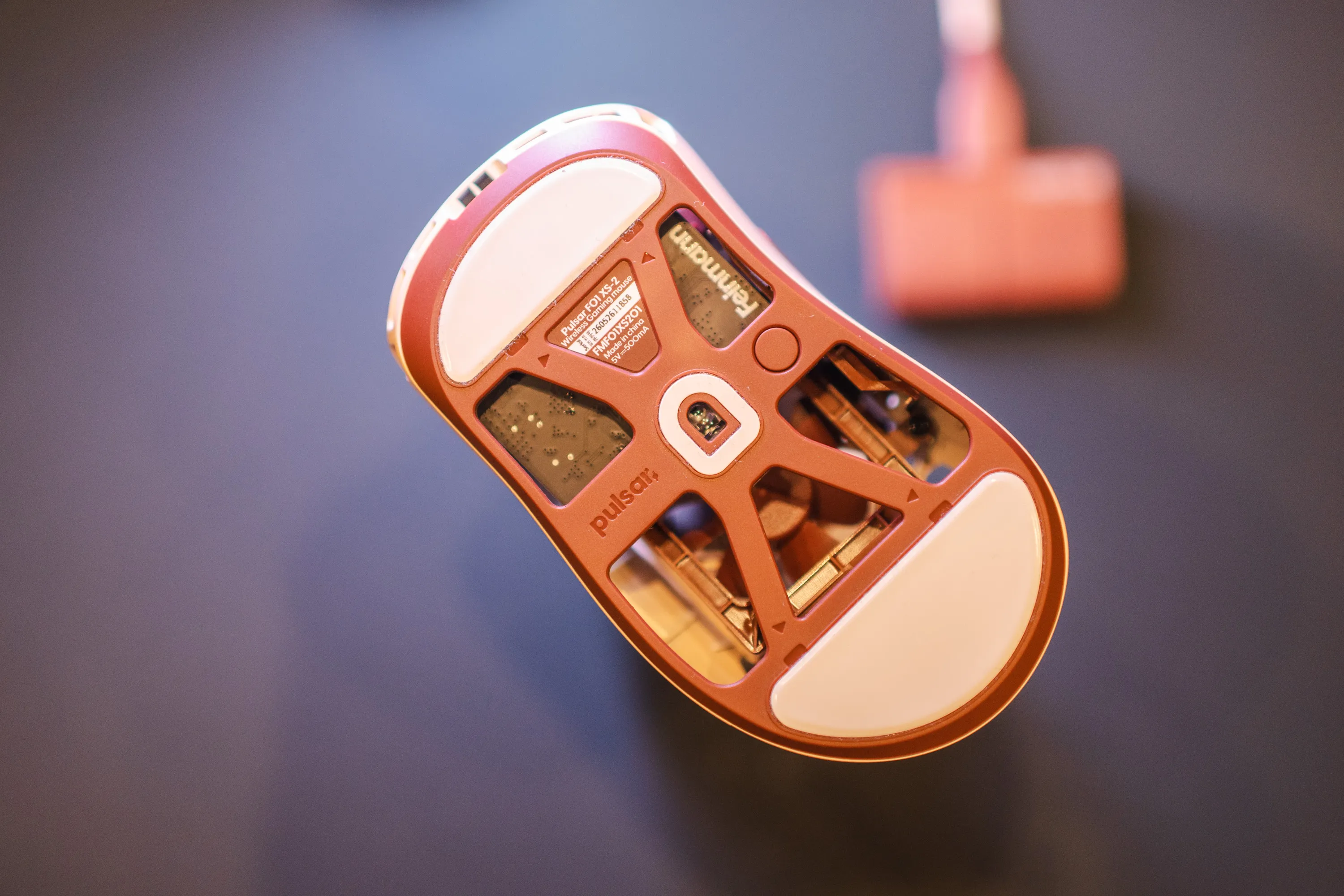 The underside of the Feinmann F01 Noctua Edition with the sensor, skates and product label, the receiver blurred in the background