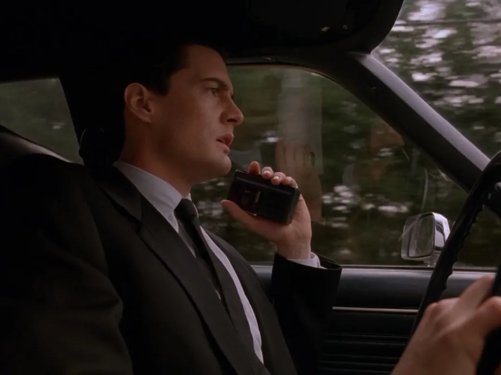 Agent Dale Cooper sitting in a car, talking into a handheld microcassette recorder