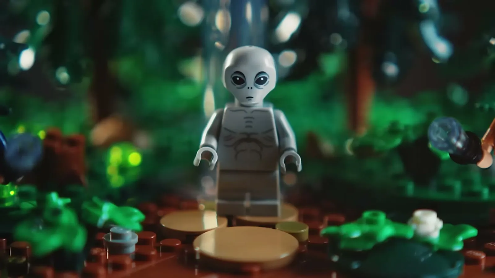 A grey alien minifigure standing in a LEGO forest lit green
