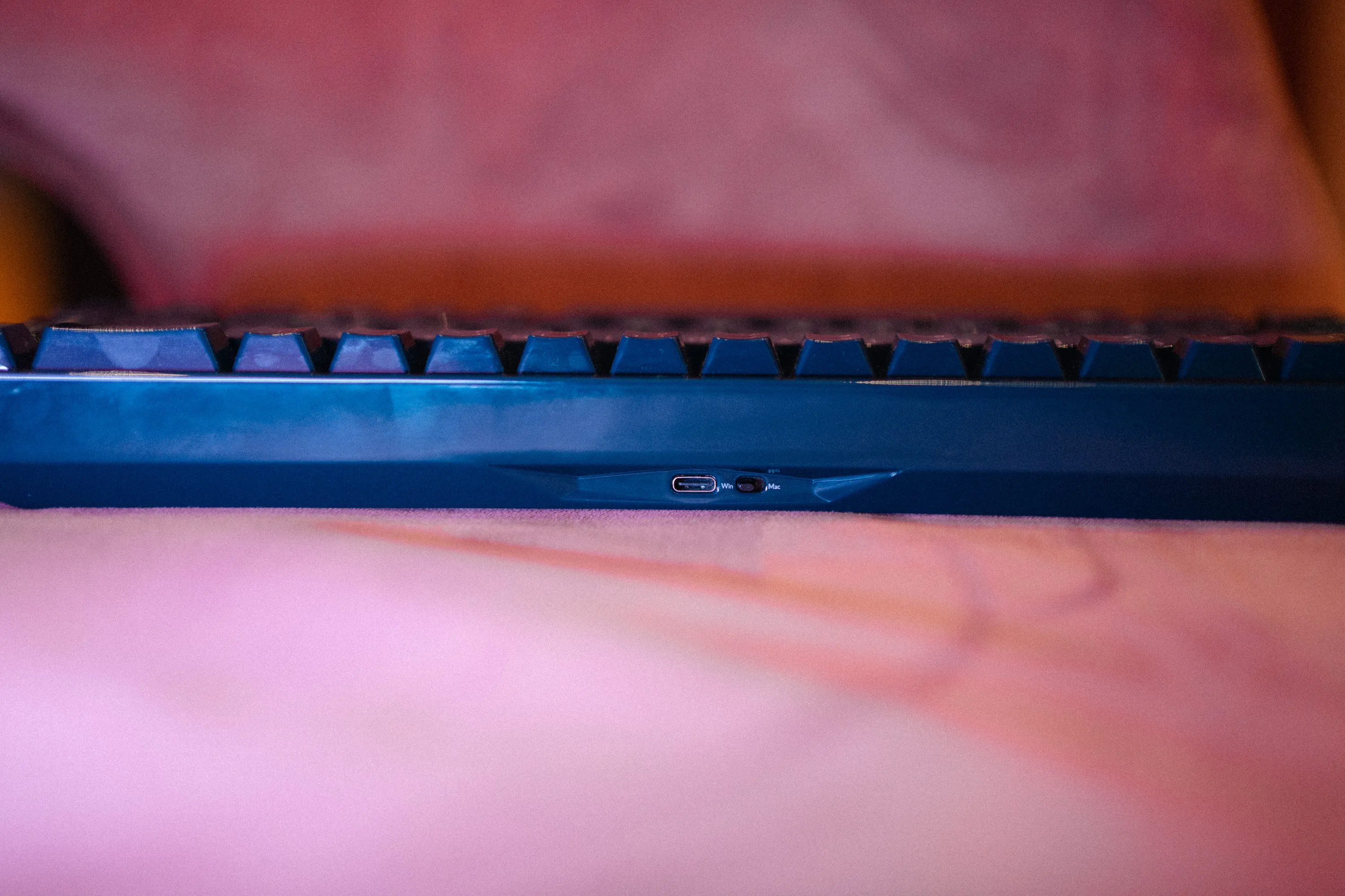 The back edge of the Keychron Q16 HE in royal blue, with the USB-C port and the Mac/Windows switch, and clear fingerprints in the glossy ceramic