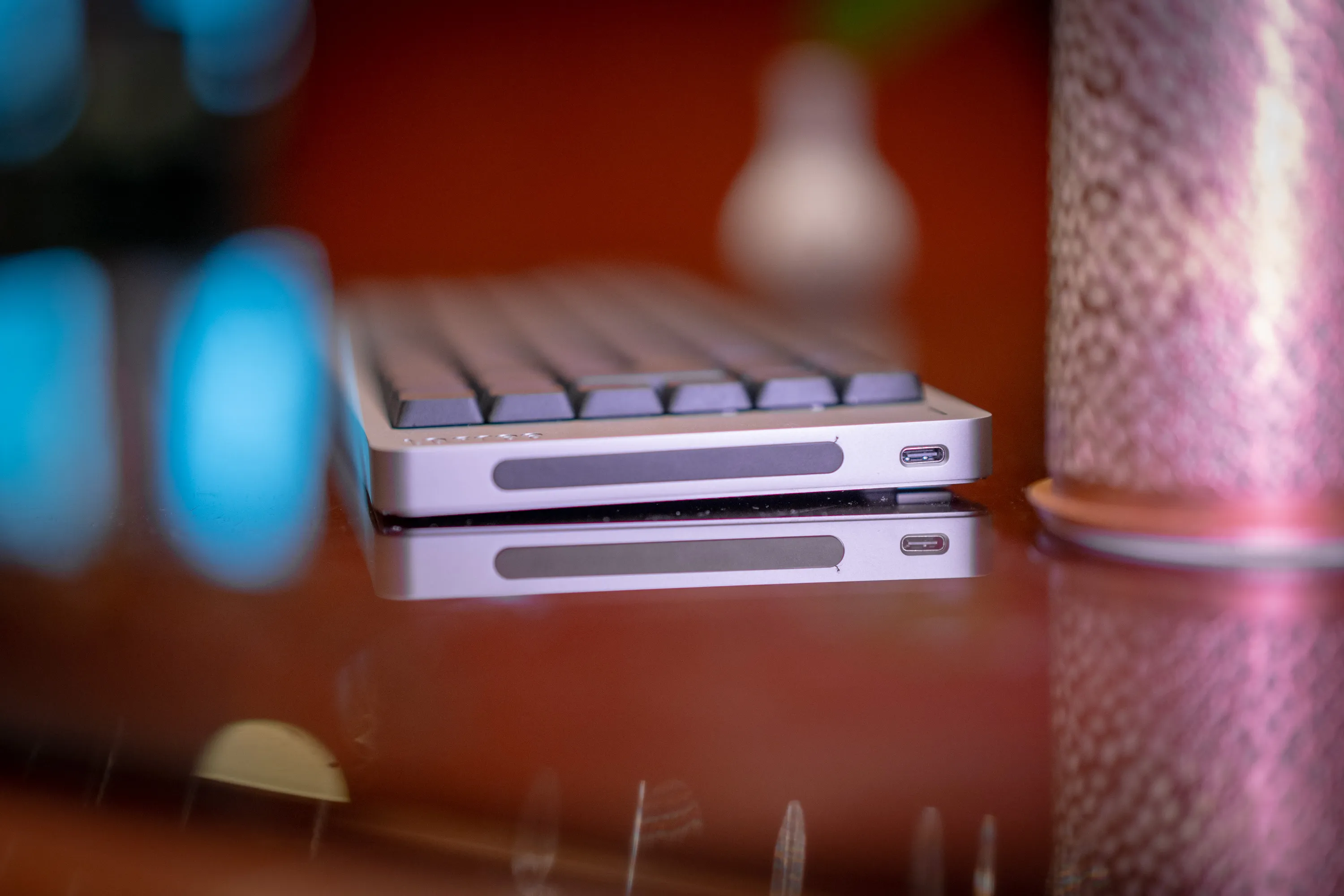 The right short side of the Lofree Flow 2 on the glass table, with the touch bar and the USB-C port mirrored in the glass