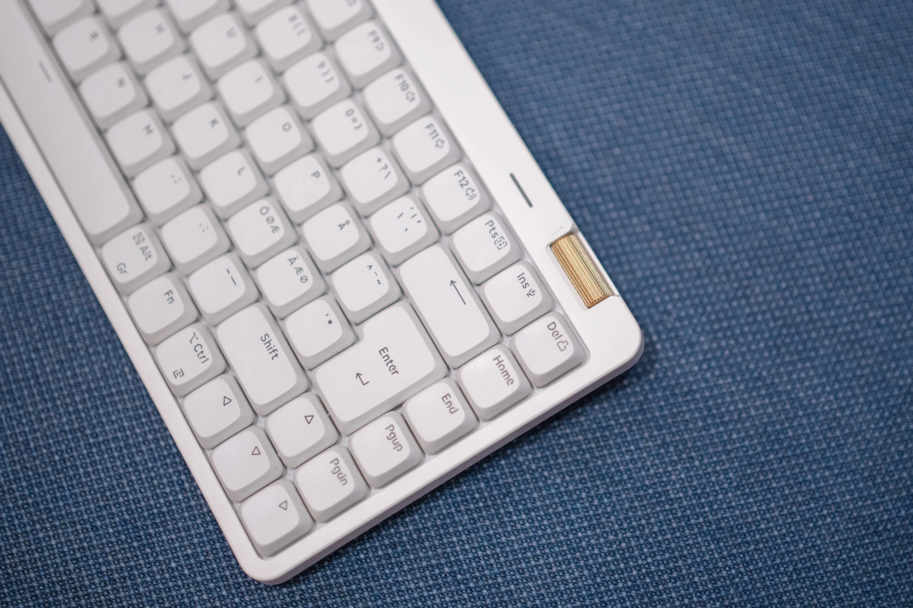 The right corner of the Lofree Flow Lite 84 in Off White on a blue fabric seat, with the brass volume roller, ISO Enter and Nordic keys with Ö, Ø and Æ