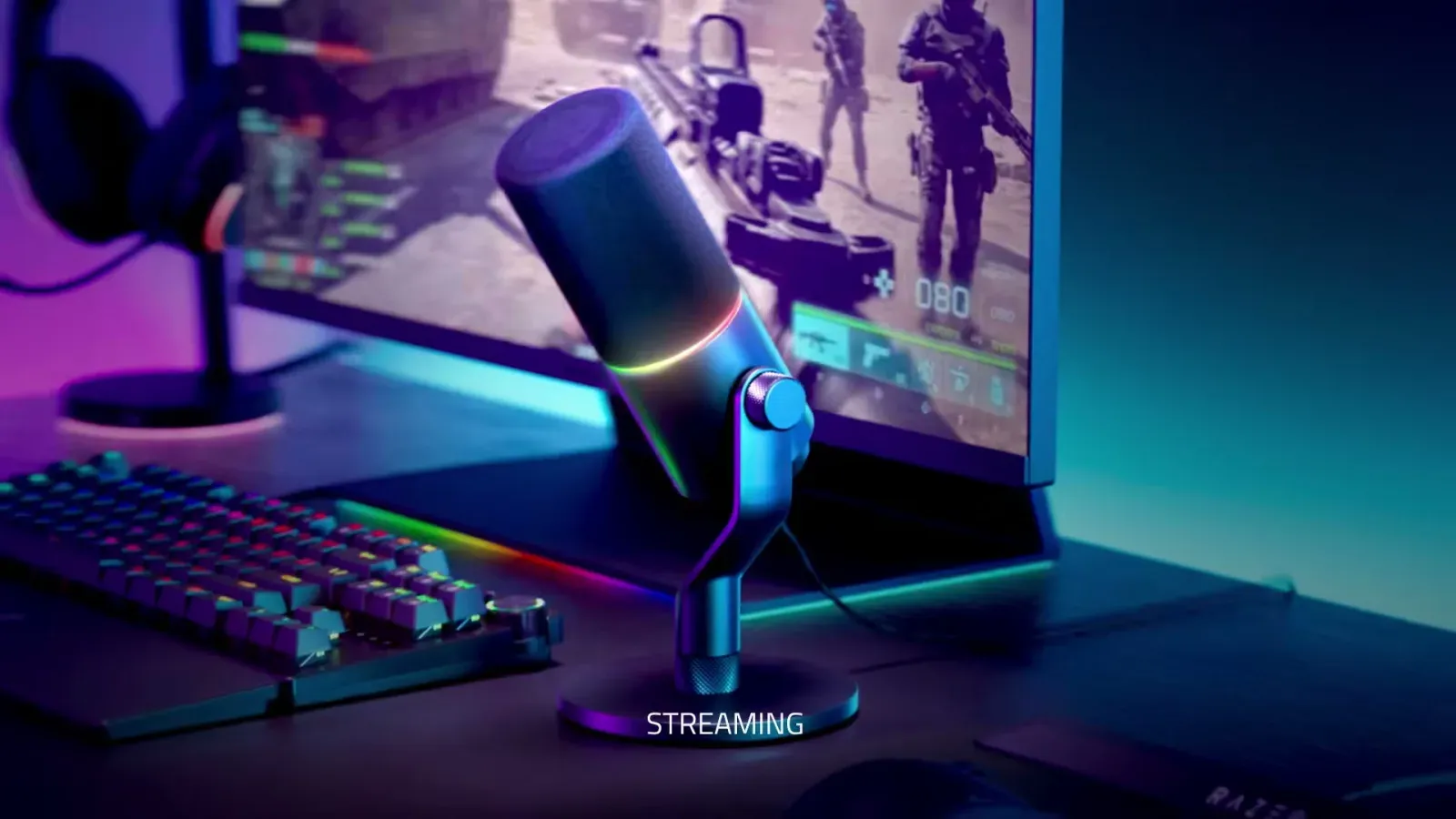 Razer Seiren V3 Pro on a desk stand next to a gaming setup with keyboard and monitor