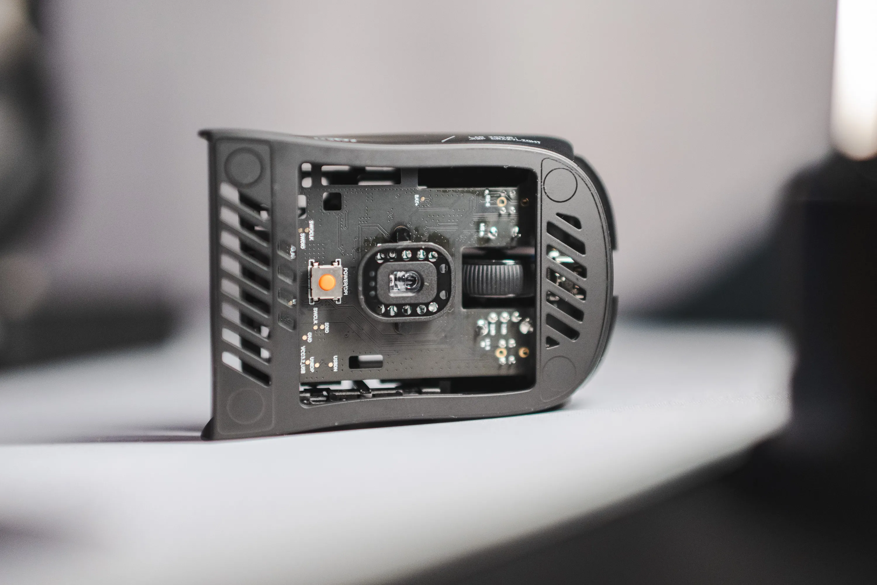 The underside of the Pulsar X2F CrazyLight standing on its edge, with the sensor, circuit board and an orange DPI button visible through the frame